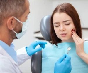 Girl with sad face in Dentist Chair touching her cheek with pain in mouth. 